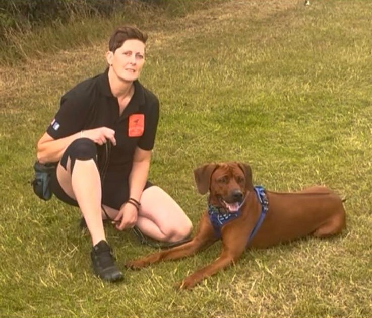 Kirstie crouched beside a relaxed brown dog on the grass